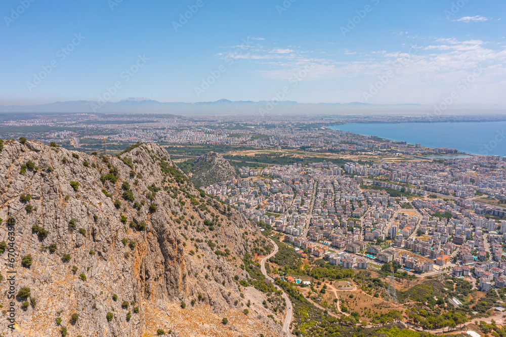 Flight over ridge mountain pass rocky terrain with bushes, bird's eye view overlooking the city, houses and buildings, roads and ships, Mediterranean coast, resort area, vacation trip.