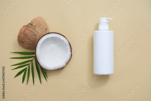 Top view of a labelless white shower gel bottle displayed with fresh coconut and green leaves on a minimalist background. The image is suitable for advertising cosmetics extracted from coconut. photo