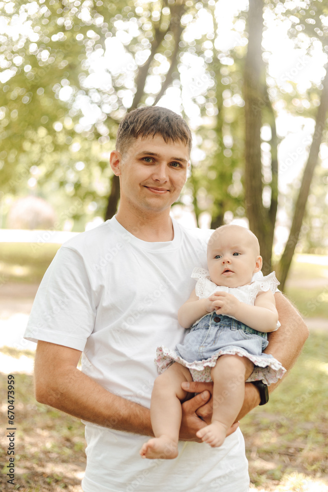 Dad's day. Smiling cute dad carefully holds his newborn daughter in his arms onsummer day outside. Dad's day. Smiling cute dad carefully holds his newborn daughter in his arms onsummer day outside.