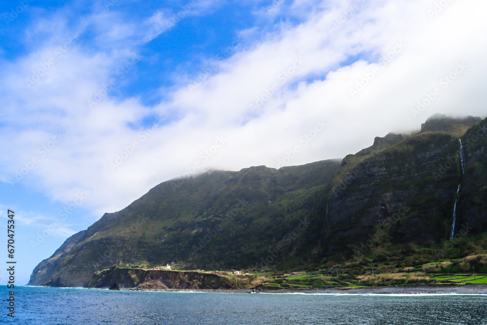 Impressive waterfall drops from a high cliff creating a small lake at its bottom. Cascata do Poço do Bacalhau. Huge cascade in front of ocean. European Hawaii.