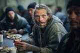 Adult caucasian male with long hair and tattoos holding a cup, surrounded by other people. The concept of homeless people.
