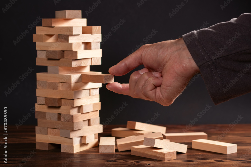 Closeup hand man take one block on The tower from wooden blocks Closeup hand man take one block on The tower from wooden blocks