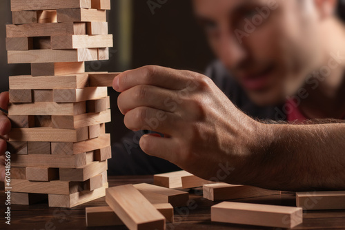 man hands making stack of wooden blocks for jenga game on dark brown table, while staying home during quarantine,