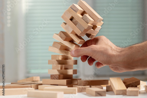 Businessman removing wooden block from falling tower on table. photo