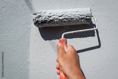 Pintor a pintar uma parede exterior com o seu rolo de pintar