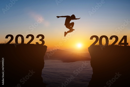 Happy new year 2024 concept. Silhouette of man jump on the cliff between 2023 to 2024 years over sunset or sunrise background. photo
