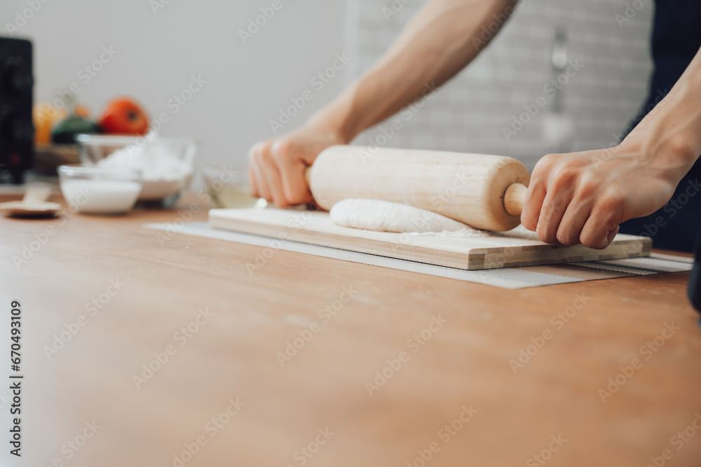 man in apron rolling out dough for homemade pastry, enjoying preparing biscuit cookies in modern light kitchen.