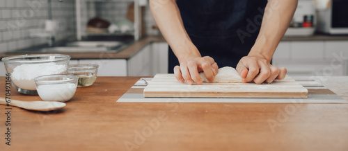 Hands knead the dough on a board for baking bread in the kitchen