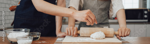 man in apron rolling out dough for homemade pastry, enjoying preparing biscuit cookies in modern light kitchen.