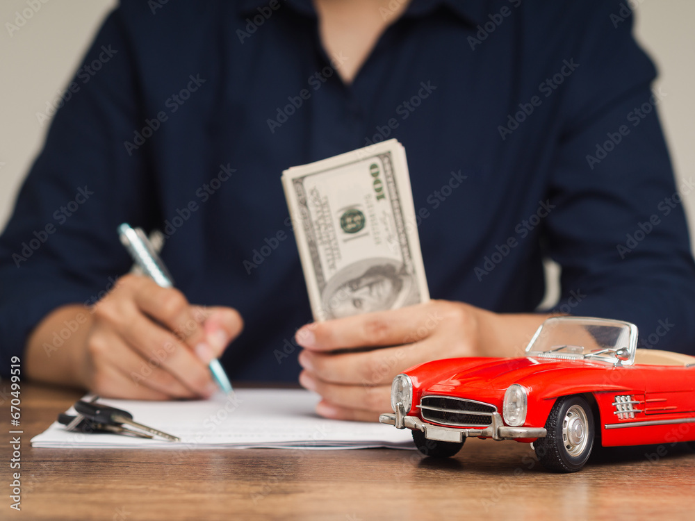 Fototapeta premium Young man in a blue shirt is filling out a car lease contract at a dealership.