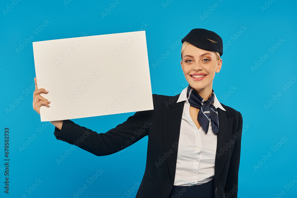 young cheerful stewardess in elegant uniform standing with empty poster on blue studio backdrop young cheerful stewardess in elegant uniform standing with empty poster on blue studio backdrop