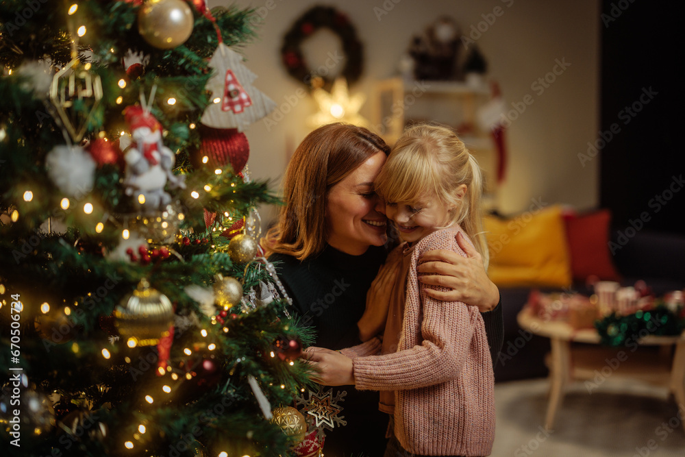 Mother and her happy daughter decorating a Christmas tree - obrazy, fototapety, plakaty 