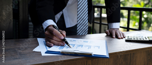 Businessmen bookkeeper hand holding pen and use calculator, laptop analysis the graph for Setting challenging business goals and ready to achieve target at home office