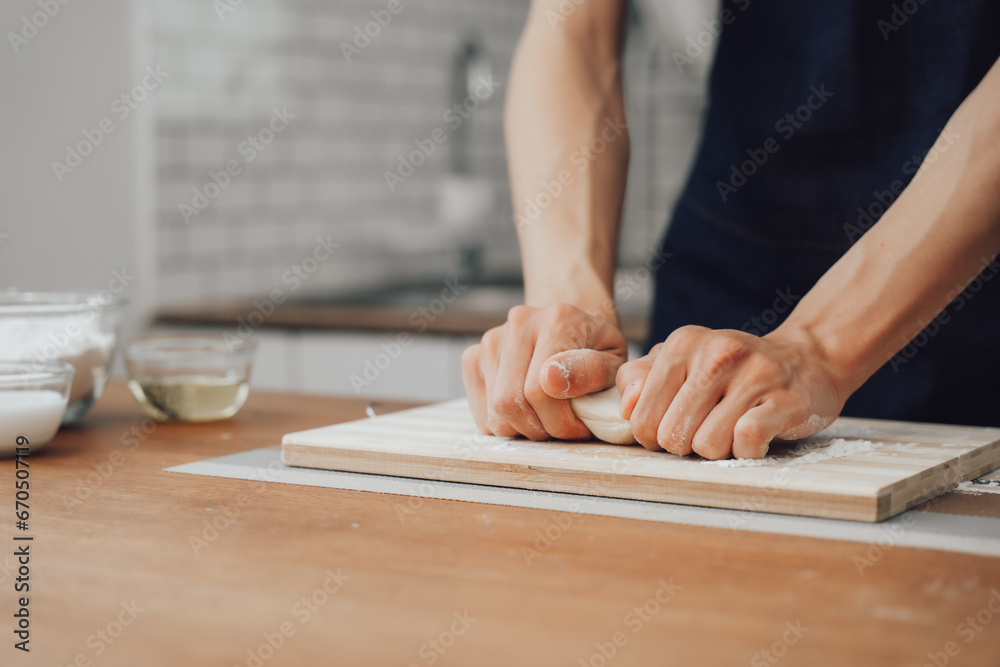 Cropped image of man wearing aprons preparing homemade pastry, kneading dough with a rolling pin on wooden table in kitchen Cropped image of man wearing aprons preparing homemade pastry, kneading dough with a rolling pin on wooden table in kitchen