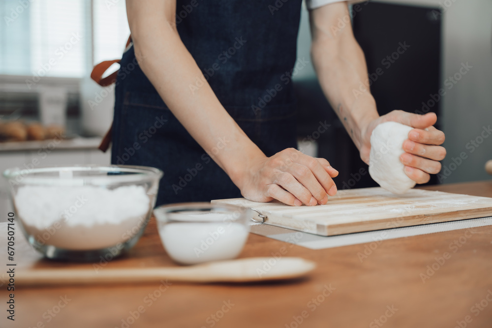 Cropped image of man wearing aprons preparing homemade pastry, kneading dough with a rolling pin on wooden table in kitchen Cropped image of man wearing aprons preparing homemade pastry, kneading dough with a rolling pin on wooden table in kitchen