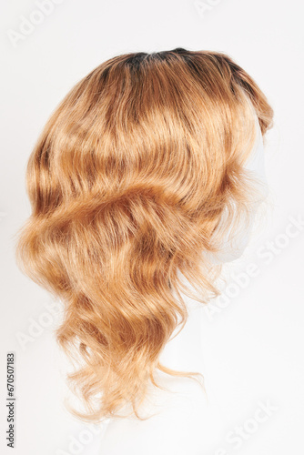 Natural looking blonde fair wig on white mannequin head. Middle length hair cut on the plastic wig holder isolated on white background, side view.