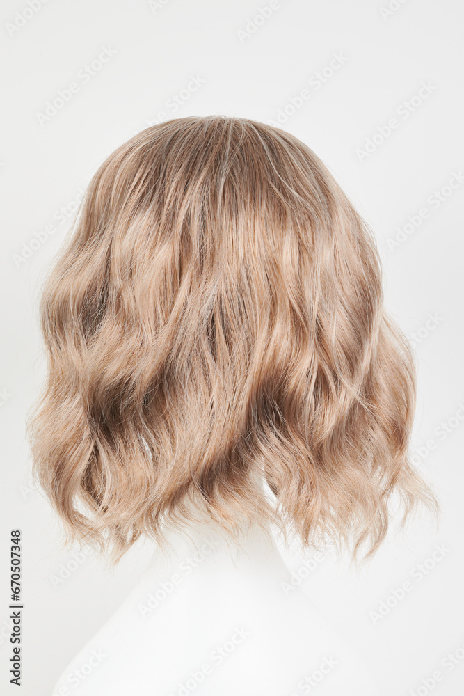 Naklejka premium Natural looking blonde fair wig on white mannequin head. Middle length hair cut on the plastic wig holder isolated on white background, back view