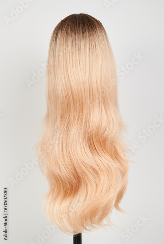 Natural looking blonde wig on white mannequin head. Long hair on the plastic wig holder isolated on white background, back view.