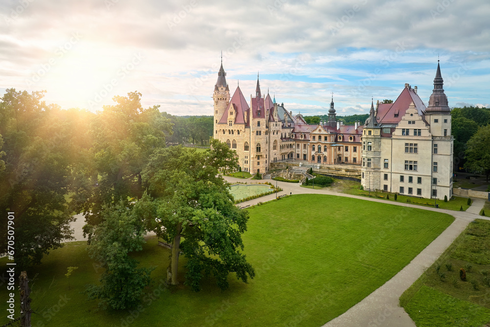 Moszna Castle from above: a fairytale castle with many towers, surrounded by a park, nicknamed the Polish Hogwarts against sunset sky.
