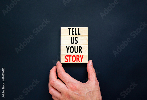 Tell us your story symbol. Concept word Tell us your story on beautiful wooden block. Beautiful black table black background. Businessman hand. Business tell us your story concept. Copy space.