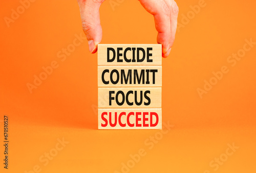 Decide commit focus succeed symbol. Concept word Decide Commit Focus Succeed on wooden block. Beautiful orange background. Businessman hand. Business decide commit focus succeed concept. Copy space.