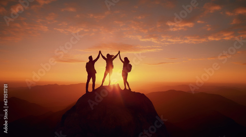 Silhouette of three people holding hands up in the air on mountain top at sunset,
