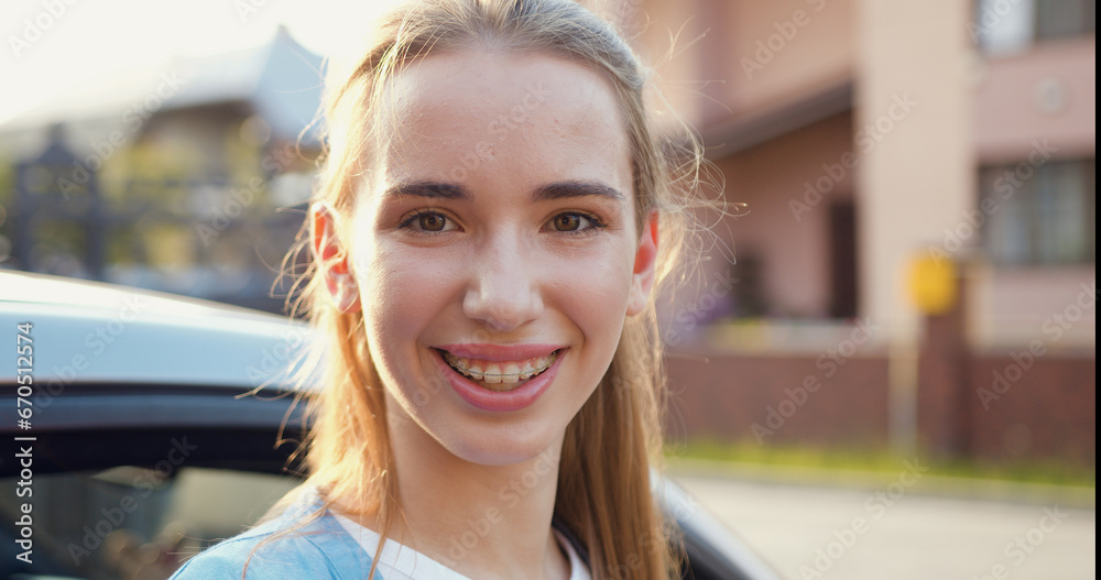 Close-up. Young beautiful girl smiles and looks at the camera against the background of pleasant sunlight at sunset. Portrait of attractive young adult stylish woman.