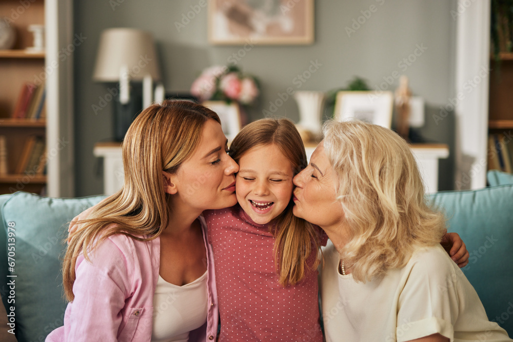 In a heartwarming snapshot, a young girl finds herself enveloped in love as her mother and grandmother affectionately kiss her cheeks. Her eyes are closed in delight, her mouth open in a joyful giggle In a heartwarming snapshot, a young girl finds herself enveloped in love as her mother and grandmother affectionately kiss her cheeks. Her eyes are closed in delight, her mouth open in a joyful giggle