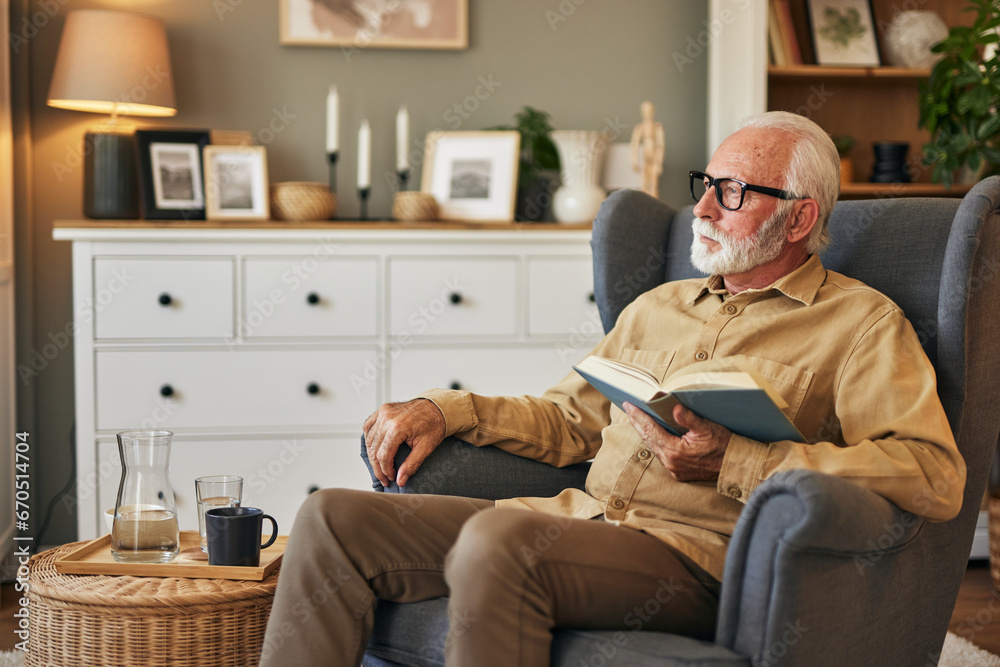 Elderly man sitting in armchair and reading a book at home Elderly man sitting in armchair and reading a book at home