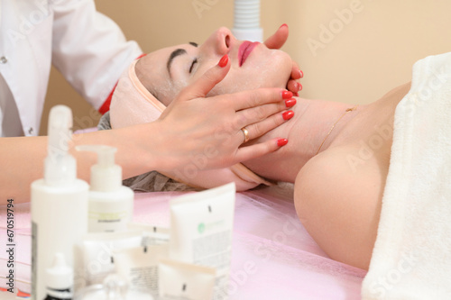 Applying cream to a woman's face with massaging movements by a beautician.