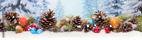 Colorful Christmas balls and lights in a row with pine cones and branches covered with snow and snowfall on abstract background in winter. Horizontal composition.