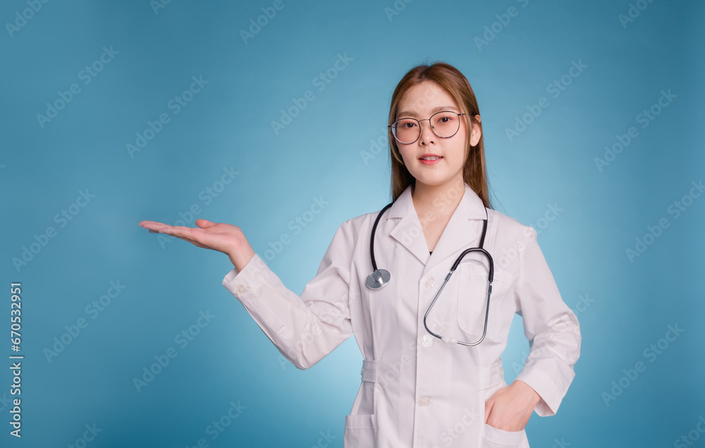 Young asian doctor wear medical uniform lab coat and stethoscope making presentation of new option on blue background. Happy doctor hold open palms novelty products advising good quality vitamins. Young asian doctor wear medical uniform lab coat and stethoscope making presentation of new option on blue background. Happy doctor hold open palms novelty products advising good quality vitamins.