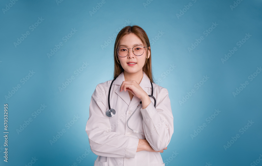 Portrait of smiling female doctor posing with arms crossed looks at camera. Young asian doctor wear medical uniform lab coat and stethoscope isolated over blue color background. Medical staff concept. Portrait of smiling female doctor posing with arms crossed looks at camera. Young asian doctor wear medical uniform lab coat and stethoscope isolated over blue color background. Medical staff concept.