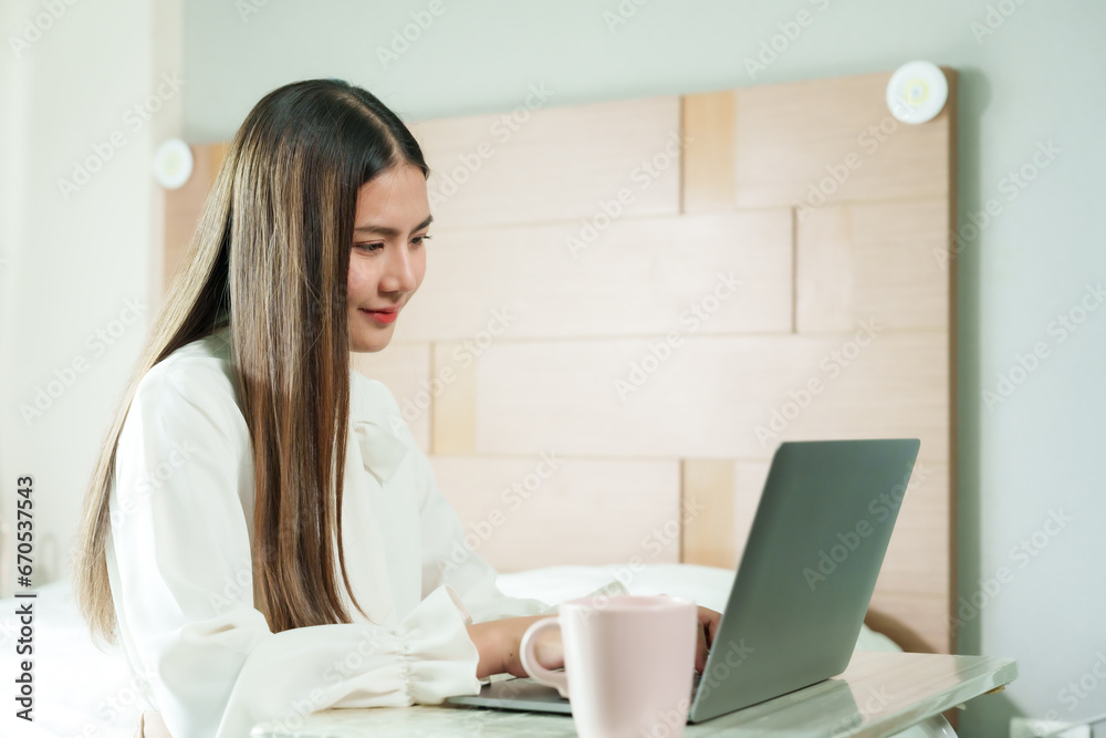 While working from home, beautiful Asian woman with long hair is thinking, sitting and typing emails on laptop computer. on bed in bedroom Prepare to send meeting minutes to supervisors on holidays. While working from home, beautiful Asian woman with long hair is thinking, sitting and typing emails on laptop computer. on bed in bedroom Prepare to send meeting minutes to supervisors on holidays.