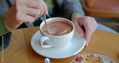 Girl hand stirs hot chocolate in white cup with spoon.