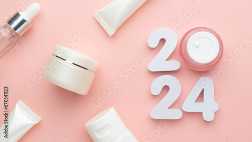 Best skincare products and cosmetic trends of 2024 concept. 2024 white number with lip balm, cream bottle, serum and lotion on pink background. photo