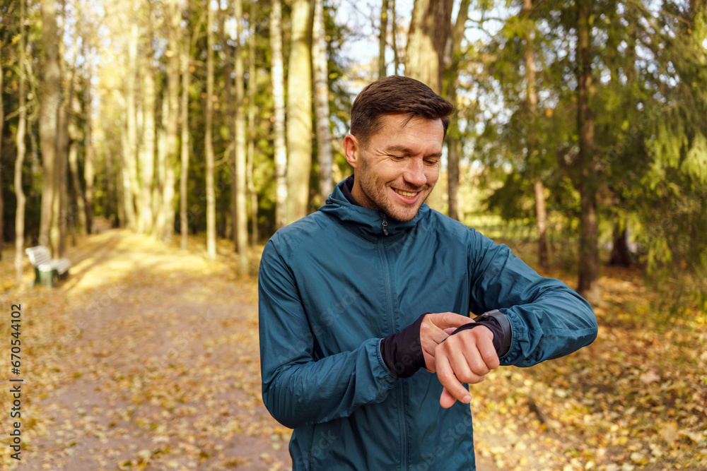 Looks at the result and progress of the workout in hours. Training in autumn and winter in the cold, warm clothes for street sports. A man also acquires mental health with daily training. Looks at the result and progress of the workout in hours. Training in autumn and winter in the cold, warm clothes for street sports. A man also acquires mental health with daily training.