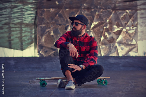 Bearded hipster sitting on longboard at skate park