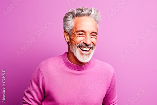 Homme sénior riant avec un pull rose sur un fond rose © Concept Photo Studio