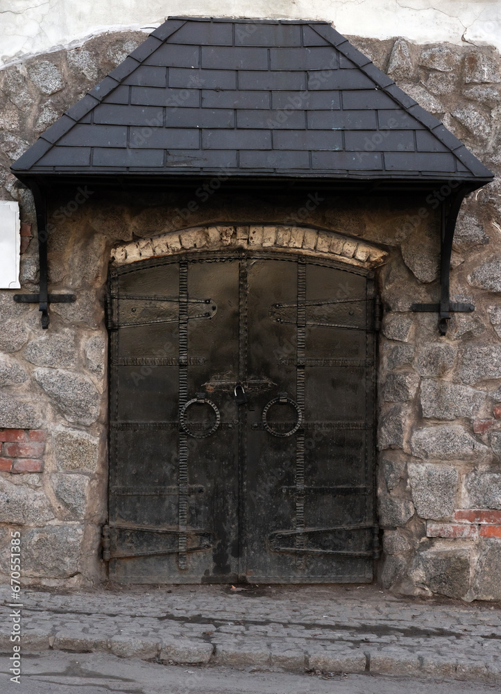 Black metal door is under a canopy in old stone wall