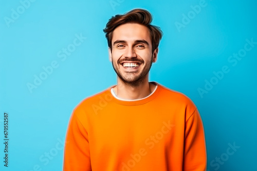 Homme sympathique avec une barbe posant avec un pull orange sur un fond bleu