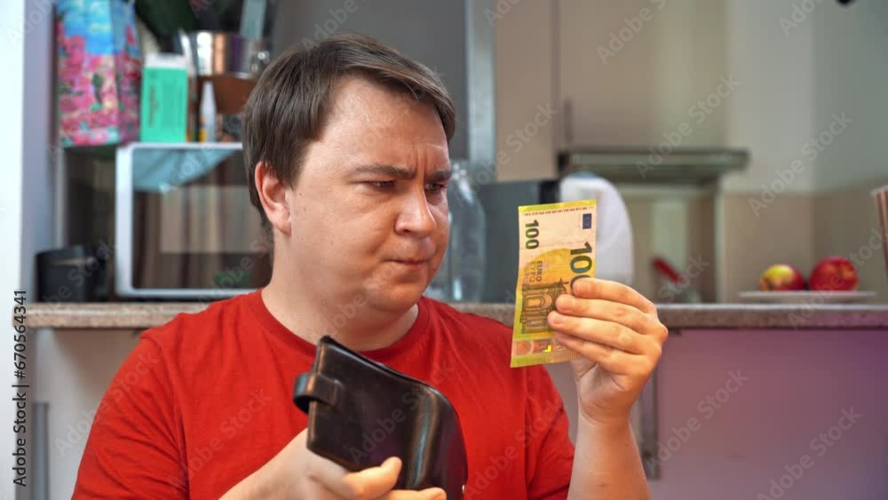 Young man in red T-shirt frowns while handing over euro banknote for home services. Man discouraged with cost of maintenance gives last money