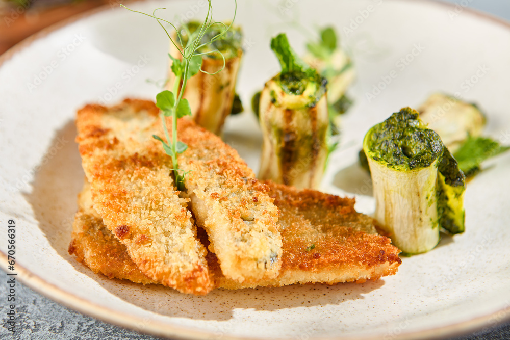 Closeup from a side view of a grilled perch fillet with zucchini rolls on a ceramic plate. The gray concrete background adds a minimalist touch to this gourmet dish Closeup from a side view of a grilled perch fillet with zucchini rolls on a ceramic plate. The gray concrete background adds a minimalist touch to this gourmet dish