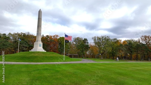 Historic Revolutionary War monument at Newtown Battlefield State Park with American flag blowing in the wind on hillside in New York State during Autumn Fall season color 