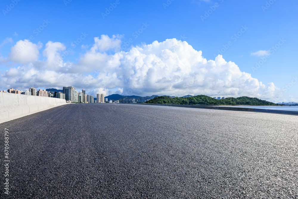 Asphalt road and city skyline with green mountain scenery under blue sky