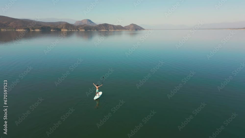Aerial drone flying over a lake, man doing stand up paddle, with mountains at sunrise. SUP. Beautifull dreamy landscape view. Cosatline with boats. Paceful landscape. Cabra Corral, Salta, Argentina. Aerial drone flying over a lake, man doing stand up paddle, with mountains at sunrise. SUP. Beautifull dreamy landscape view. Cosatline with boats. Paceful landscape. Cabra Corral, Salta, Argentina.