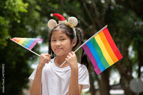Asian cute girl holds rainbow flags in public park, soft and selective focus, concept for calling out people around the world to respect gender diversity and celebration LGBT events in pride month.