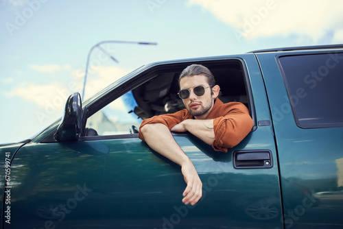 handsome young male model with sunglasses looking through car window at camera, fashion and style © LIGHTFIELD STUDIOS