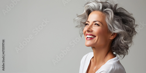 A beautiful middle-aged woman with gray hair and healthy skin is smiling in a good mood. 