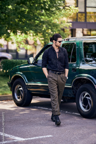 handsome sexy man with sunglasses in black shirt walking near his car and looking away, fashion © LIGHTFIELD STUDIOS
